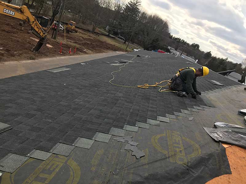 Close up of a Allsite Roofing LLC worker installing new dark gray shingles on a residential roof